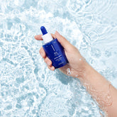 A blue glass ampoule with a dropper, labeled 'Missha Super Aqua Ultra Hyalron Ampoule in a pool of water